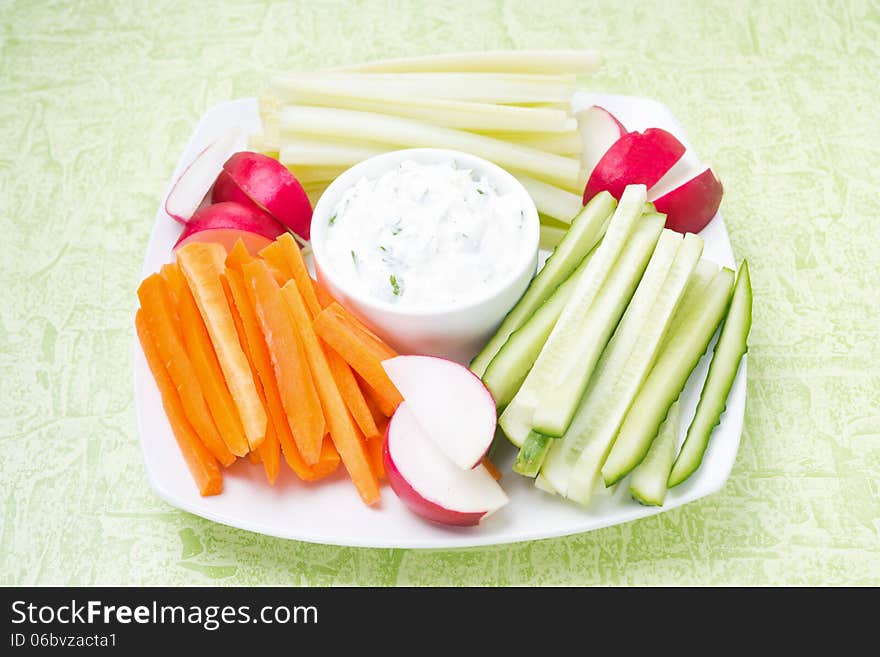 Sauce with feta cheese and assorted vegetables on a plate on green background, close-up