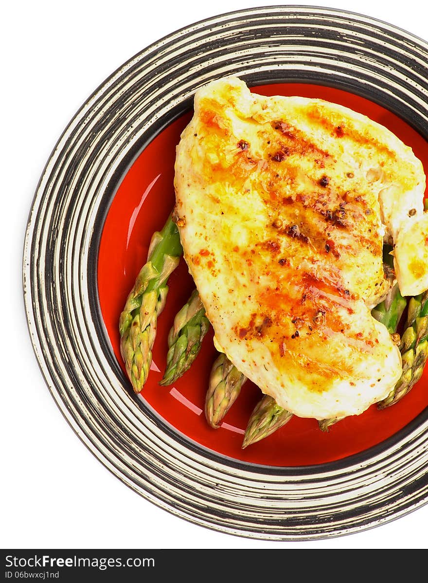 Delicious Roasted Chicken Breast with Asparagus Sprouts on Red Striped Plate closeup on white background. Top View