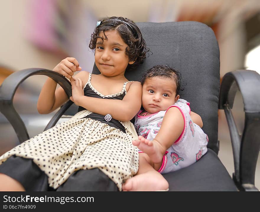 Two siblings brother & sister playing together while sitting on chair inside home. Two siblings brother & sister playing together while sitting on chair inside home