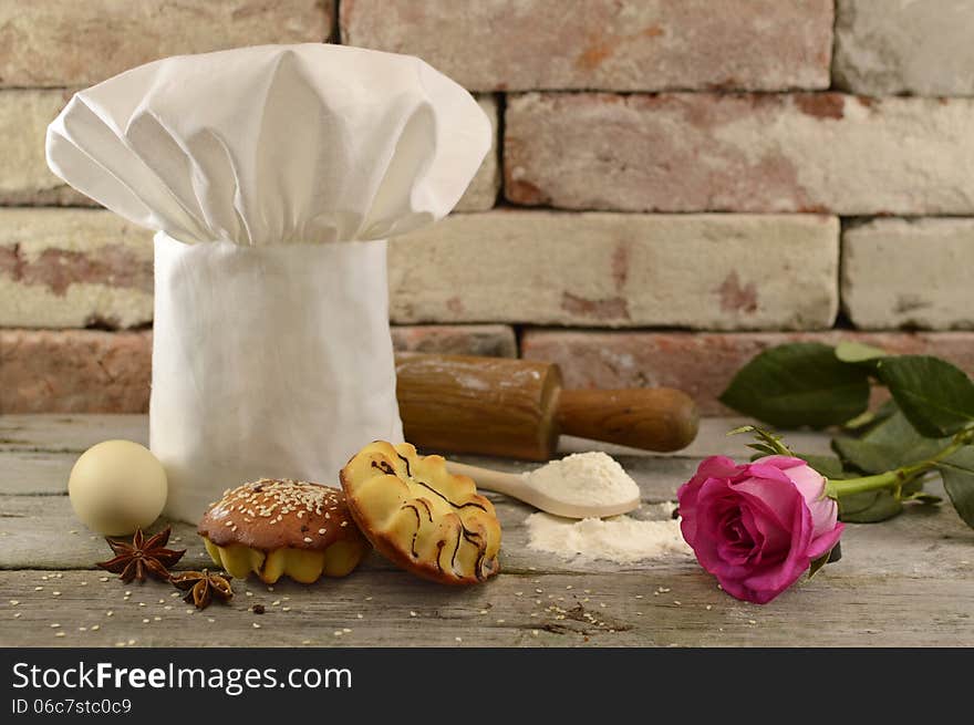 White toque with bakery, rolling pin and pink rose on brick wall. White toque with bakery, rolling pin and pink rose on brick wall