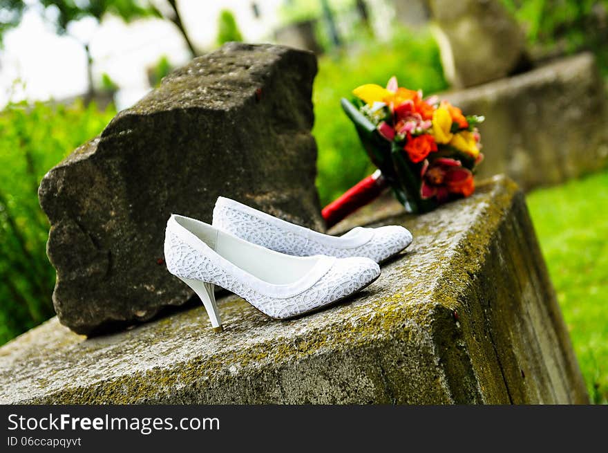 Wedding shoes with bride bouquet on a stone background