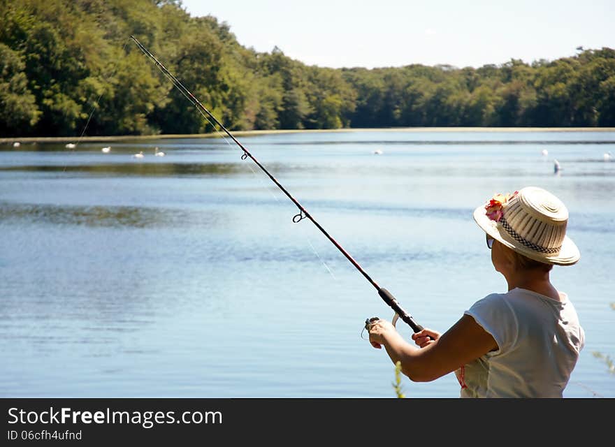 Fisherwoman on lake with rod in position ready catch fish ,swans on a distance and nice weather. Fisherwoman on lake with rod in position ready catch fish ,swans on a distance and nice weather