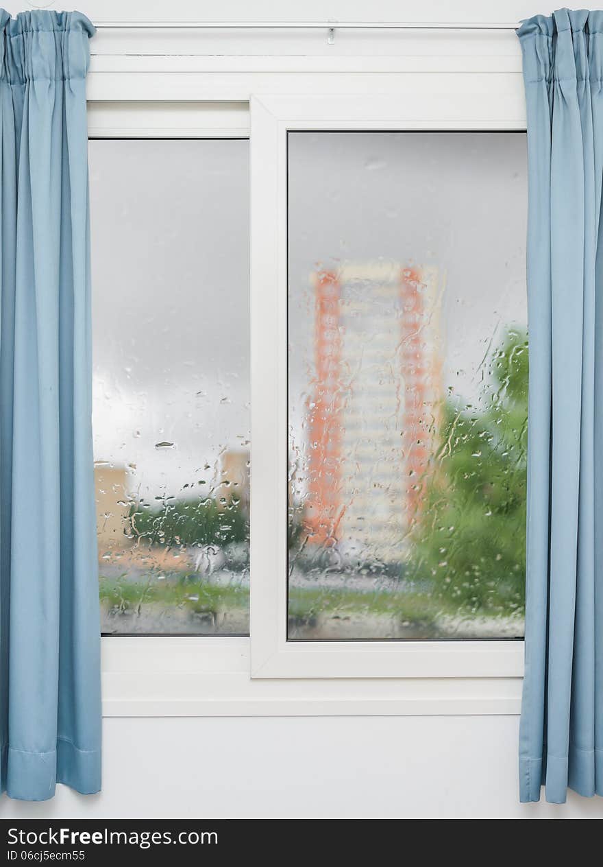 White window with blue curtains on a rainy day