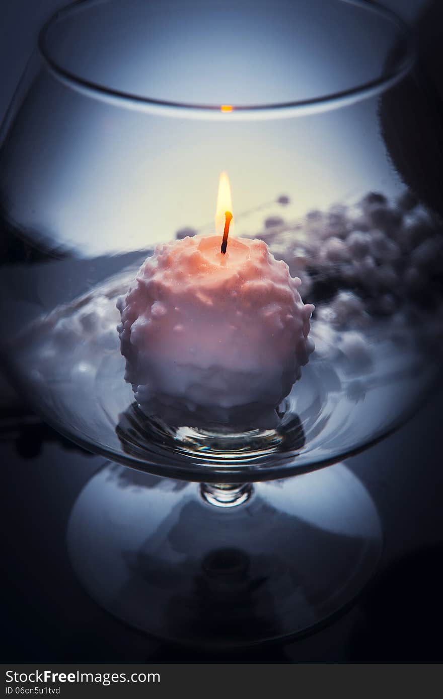 Small white candle burning and melting like a snowball inside big glass goblet. Over grey tint, blurred background. Small white candle burning and melting like a snowball inside big glass goblet. Over grey tint, blurred background.