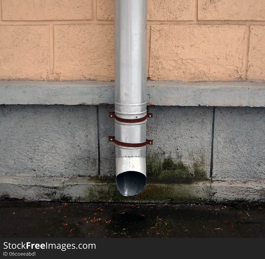 Drainpipe against a wall of a town house in cloudy weather.