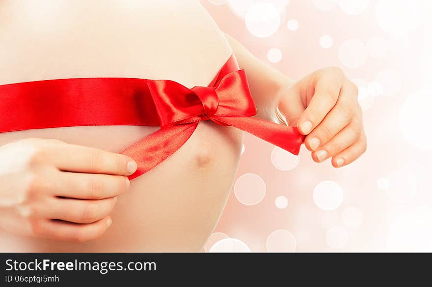 Belly of pregnant woman with red ribbon and bow