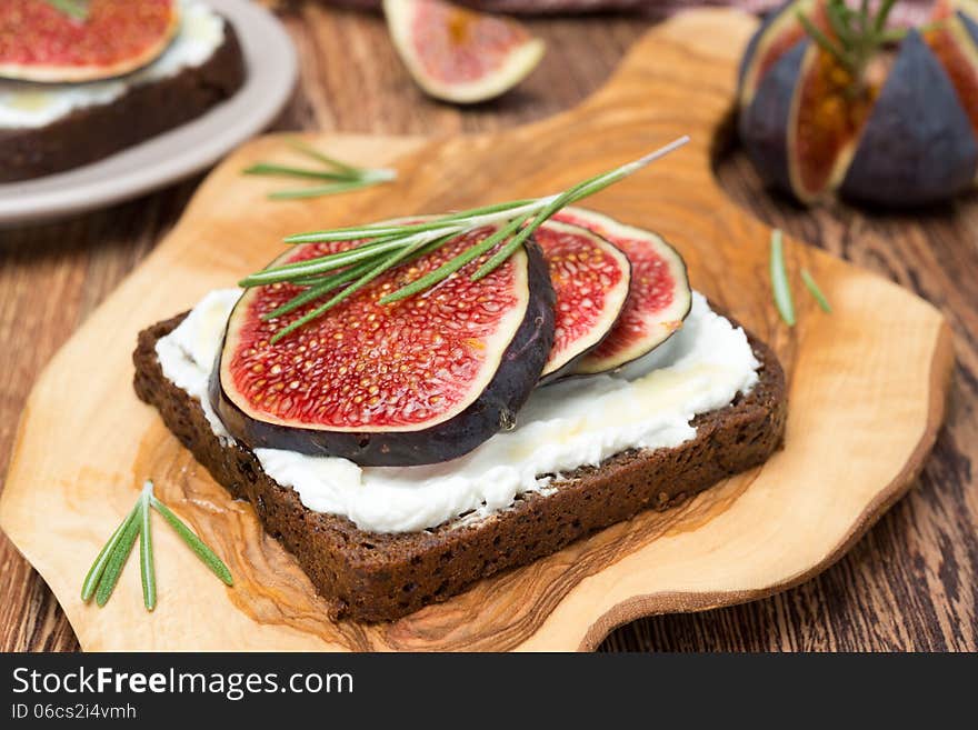 Bread with goat cheese, figs, honey and rosemary on wooden board