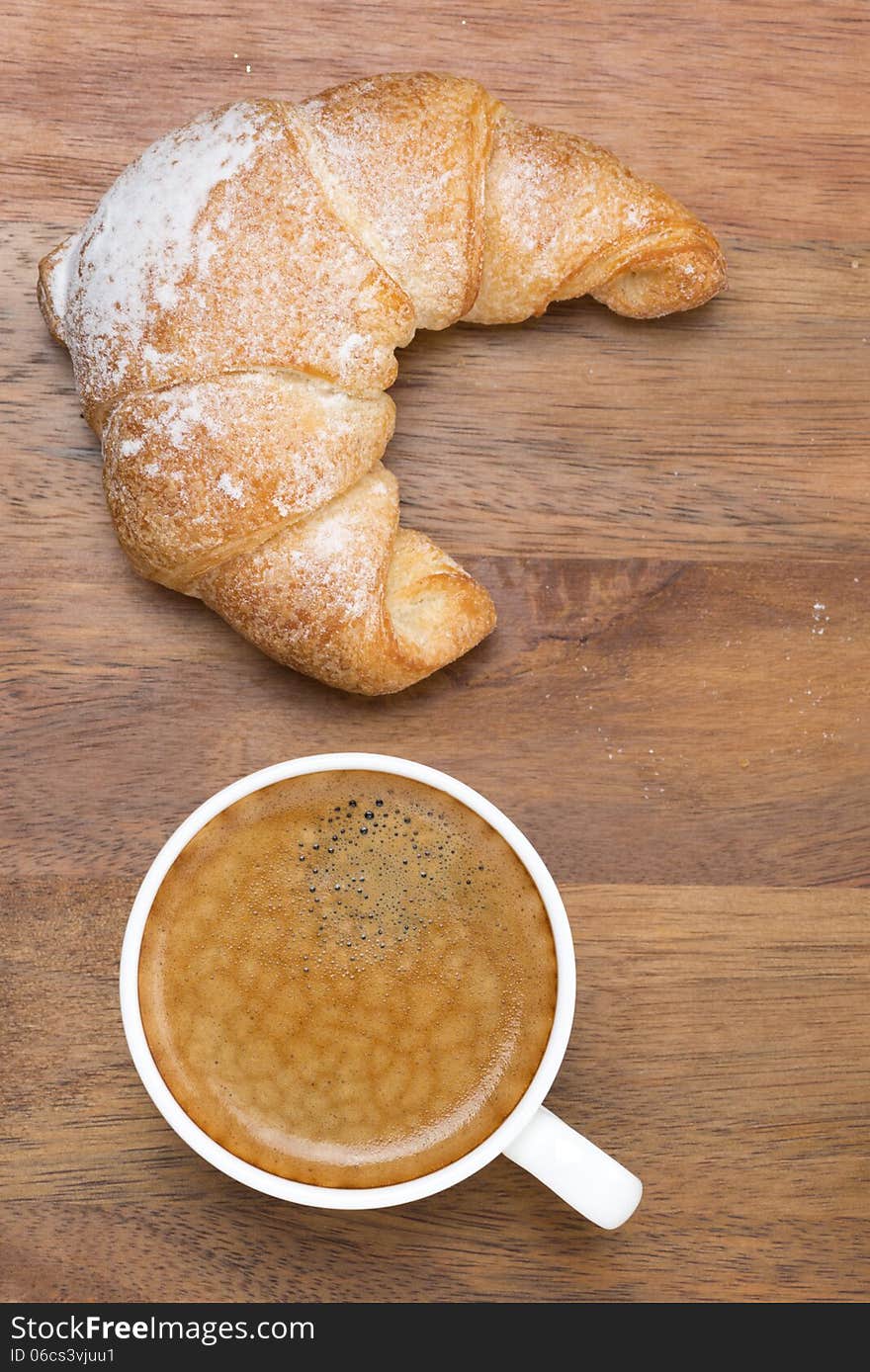 Croissant and a cup of black coffee on a wooden background