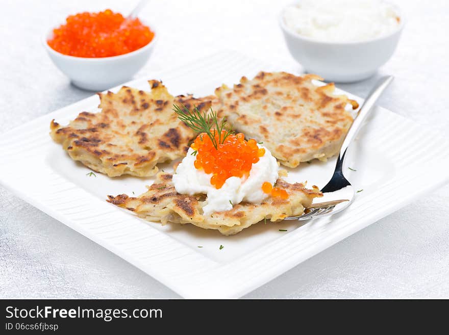 Potato pancakes with red caviar and sour cream on the plate, close-up