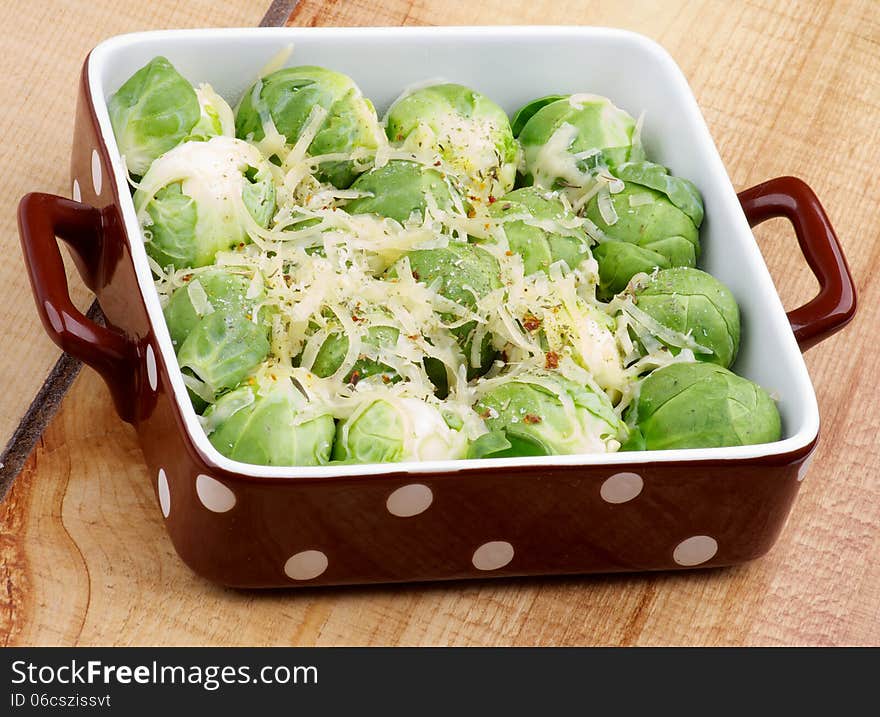 Delicious Brussels Sprouts Casserole with Grated Cheese and Spices in Brown Polka Dot Bowl closeup on Wooden background