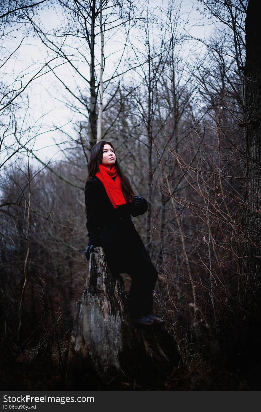 Woman in black coat and red scarf sitting in cold dark forest