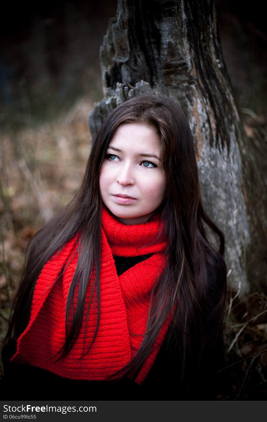 Portrait of woman in red scarf with long brunette hair in cold dark forest