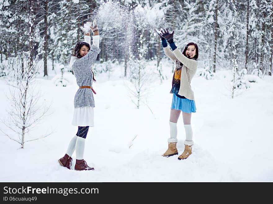 Fashion women in warm sweaters playing with snow on white forest background