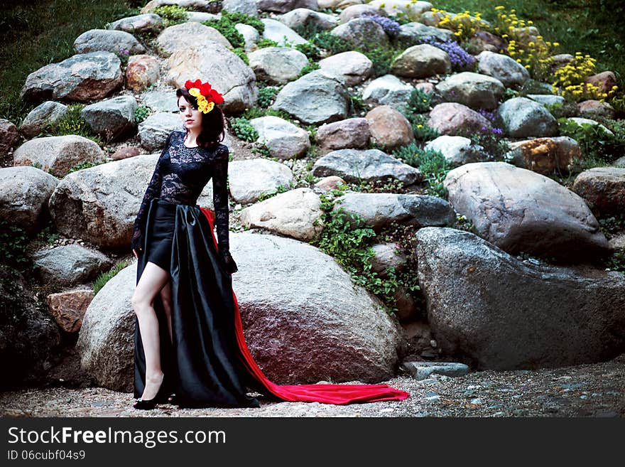 Woman in black and red lace dress and flowers on stone outdoor background full size