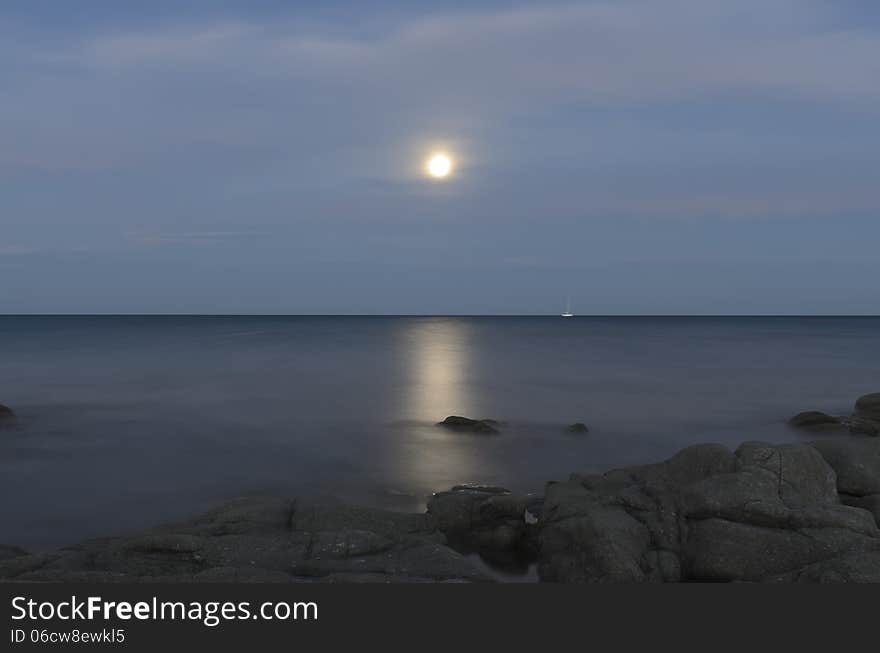 Reflections of the moon in the sea of ​​Calaliberotto, Sardinia! One of the most beautiful beach in Sardinia. Artistic view of the Moon path over the night sea with rocks and shore in the foreground. Shot with long exposure after the sunset.