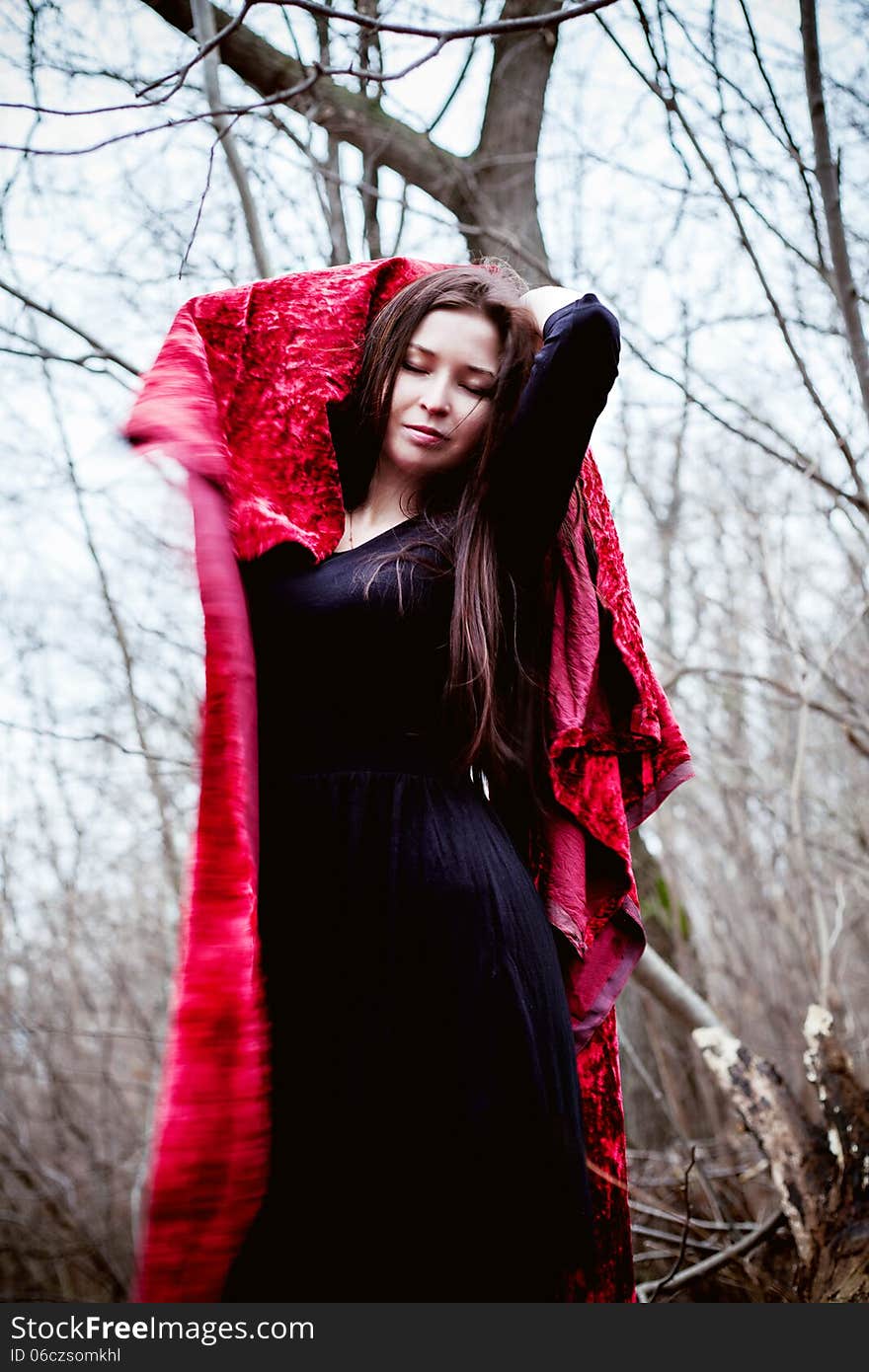 Woman in black dress with red fabric in cold dark forest