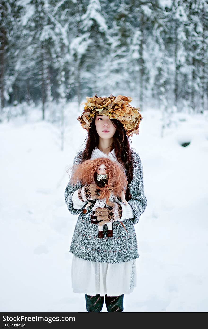 Forest woman with autumn leaves and little doll in white snow winter