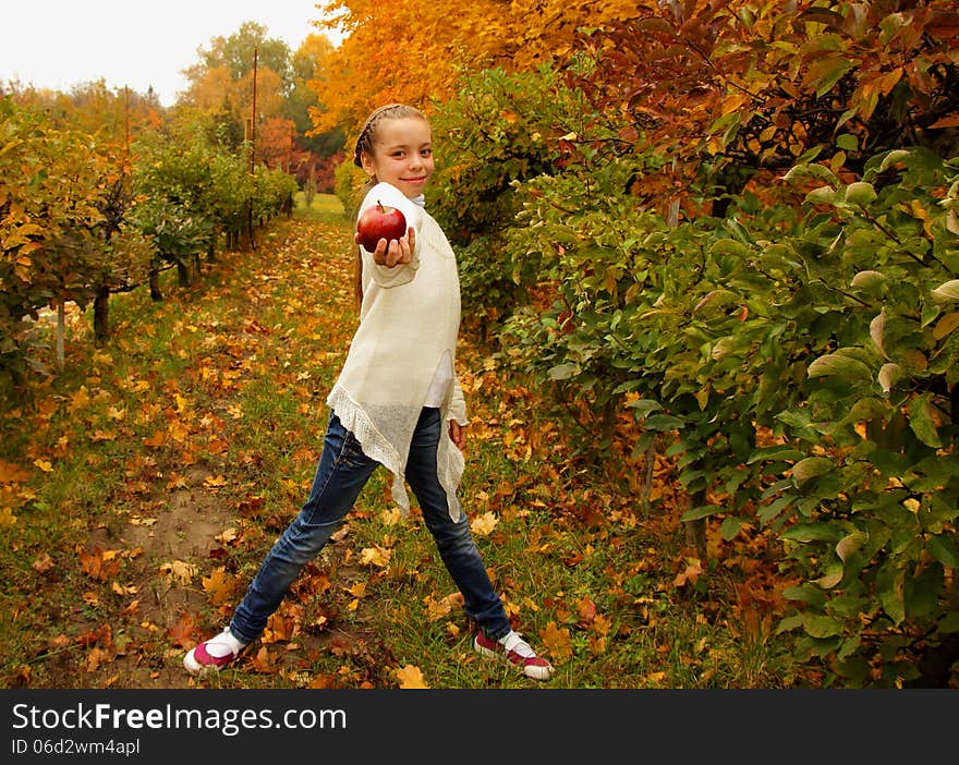 Pretty girl holding a red apple in hand on background of the autumn garden. Pretty girl holding a red apple in hand on background of the autumn garden