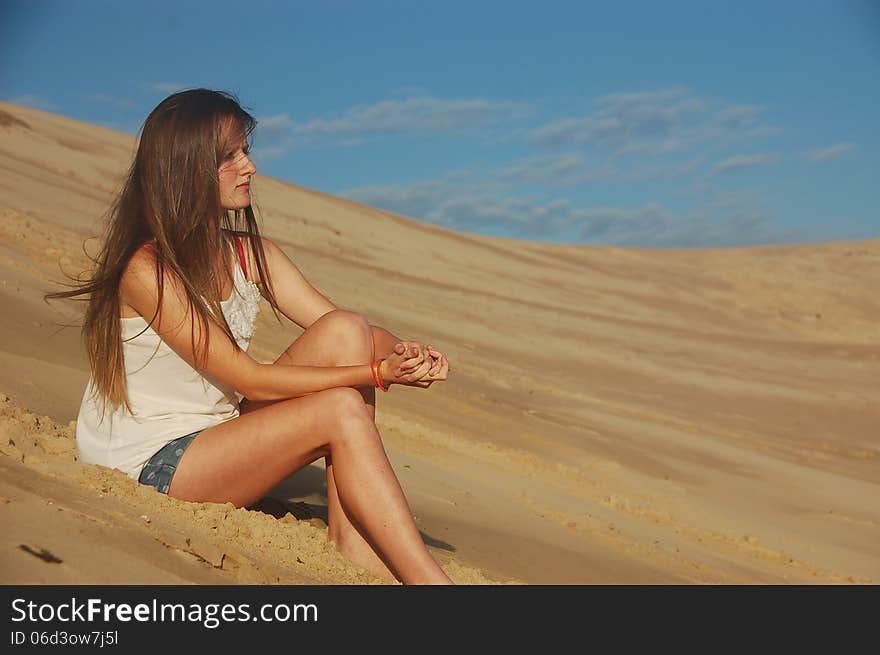 A pretty young teenager with long hair sits on a beach looking thoughtful. A pretty young teenager with long hair sits on a beach looking thoughtful.