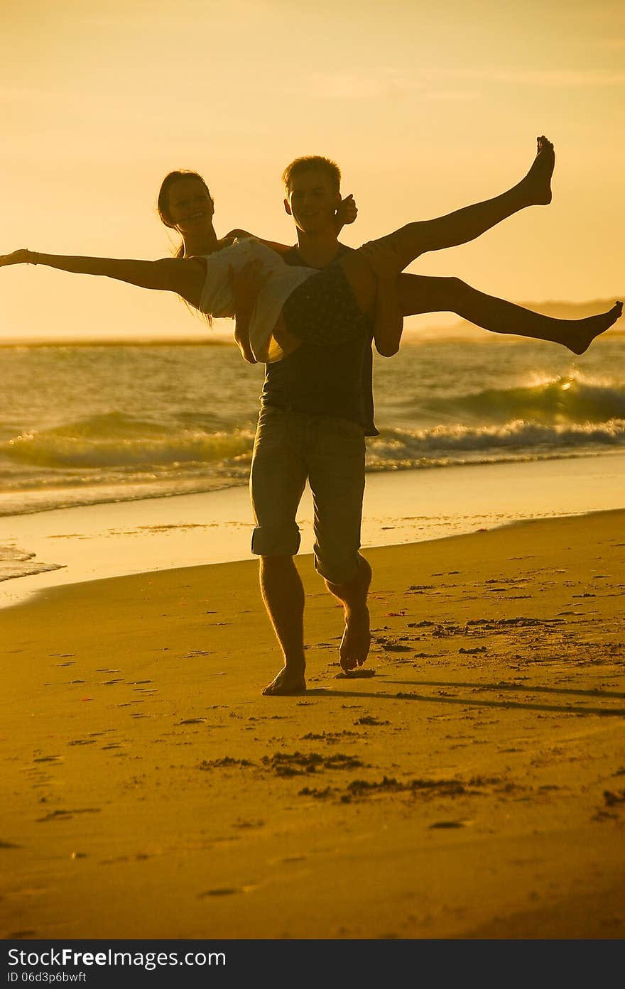 A playful young couple clown around on the beach against a yellow sunset. A playful young couple clown around on the beach against a yellow sunset.