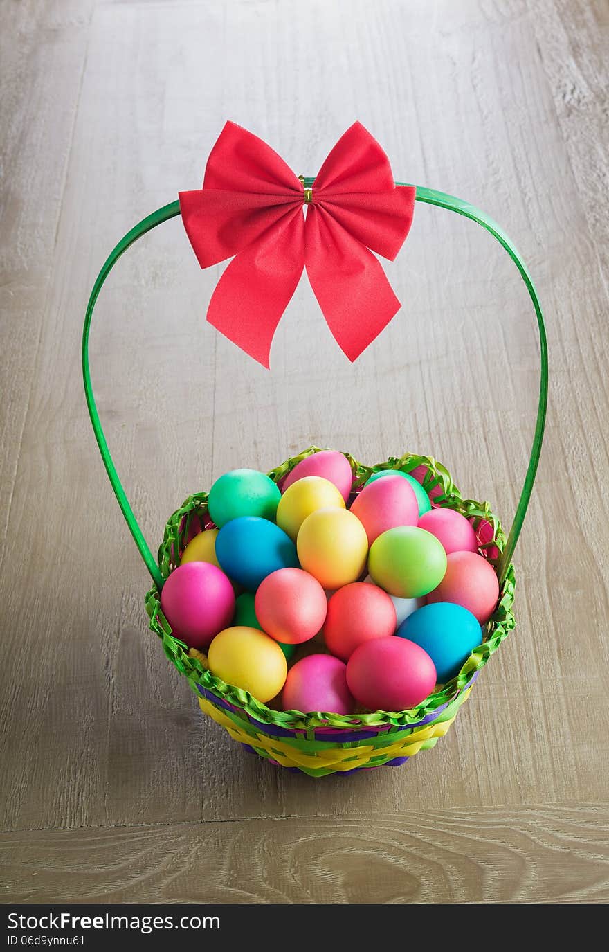 Multicolored Easter eggs in the wattled basket on vintage wooden table