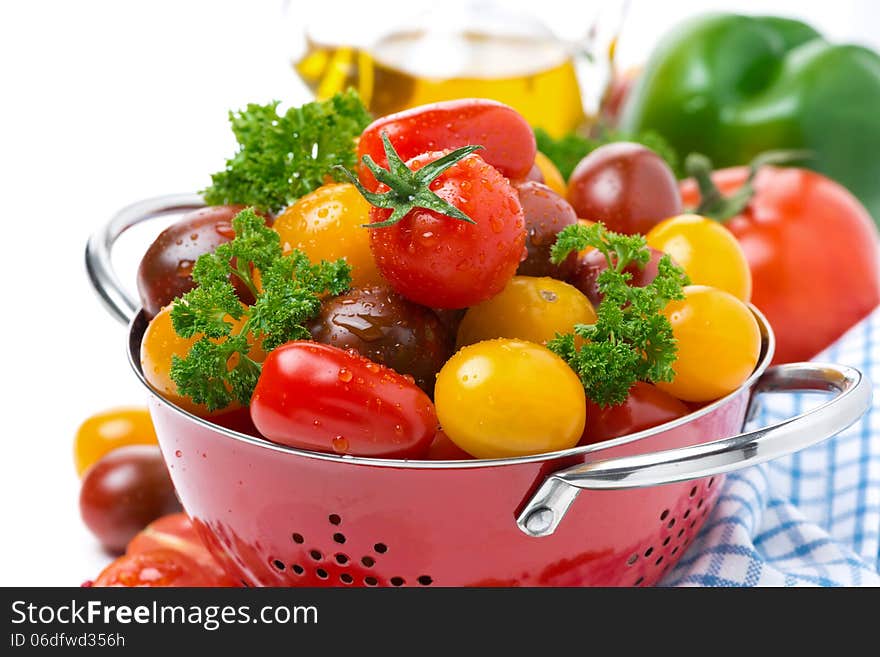 Assorted cherry tomatoes and greens in a colander, close-up