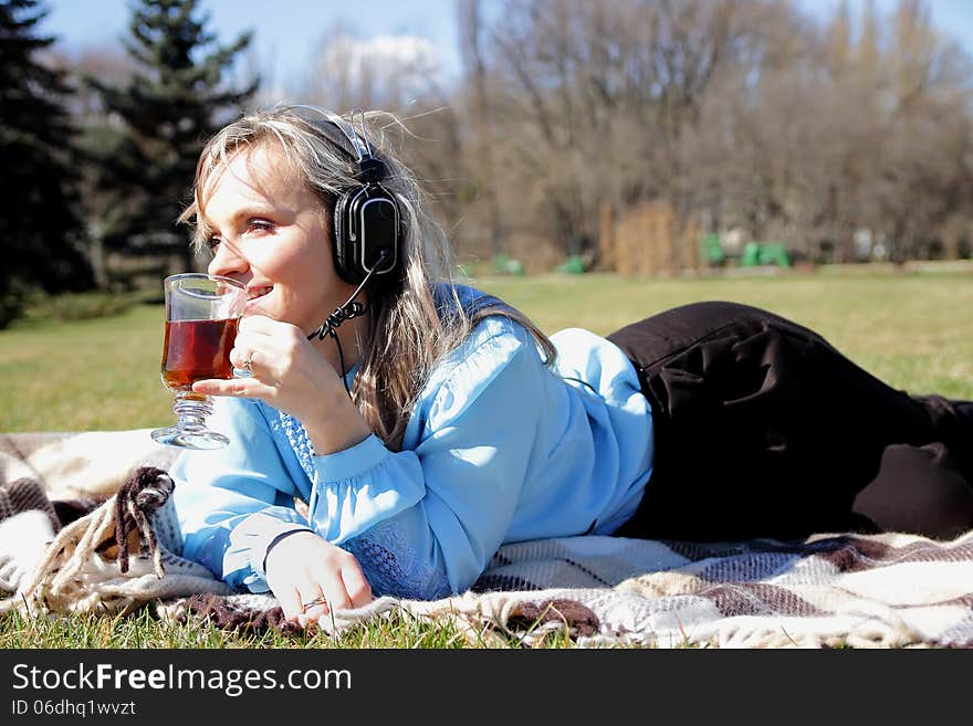 Beautiful girl on picnic listening to music in headphones and with a cup in hand