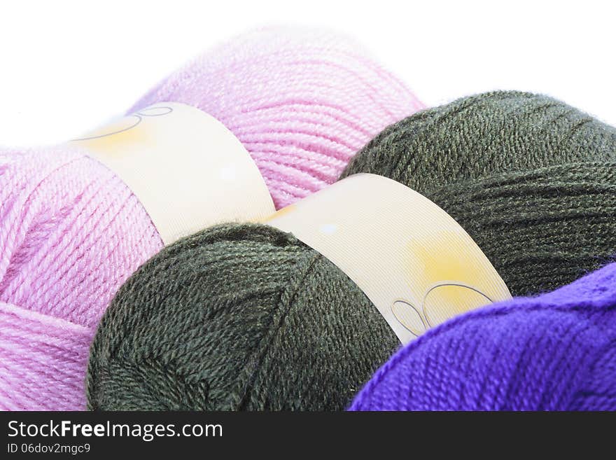 Three balls of coloured wool in pink, charcoal and purple for knitting a garment, close up view over white