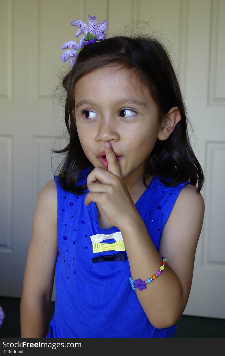 A young girl of asian descent holds her finger against her lips signalling silence. A young girl of asian descent holds her finger against her lips signalling silence.