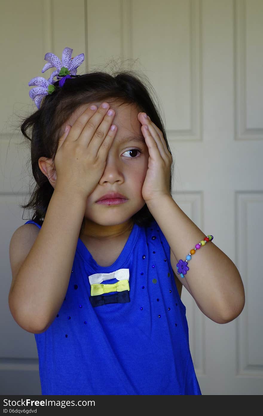 A young girl removes her hand from one eye as she looks pensively across her bedroom. A young girl removes her hand from one eye as she looks pensively across her bedroom.