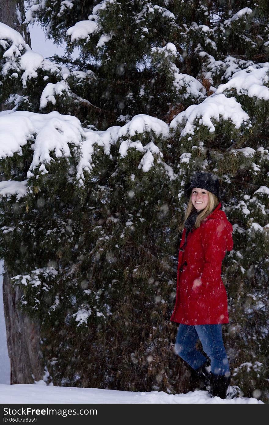 Blonde female wearing a red coat and black hat in front of trees covered in snow. Blonde female wearing a red coat and black hat in front of trees covered in snow.