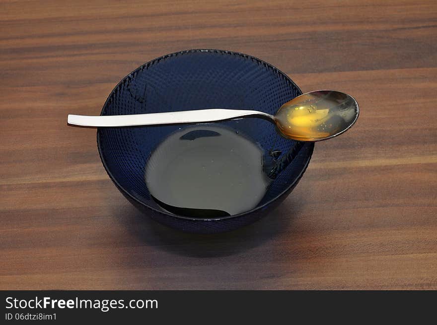 A small cup of honey with a spoon also filled with honey on a wooden table. A small cup of honey with a spoon also filled with honey on a wooden table.