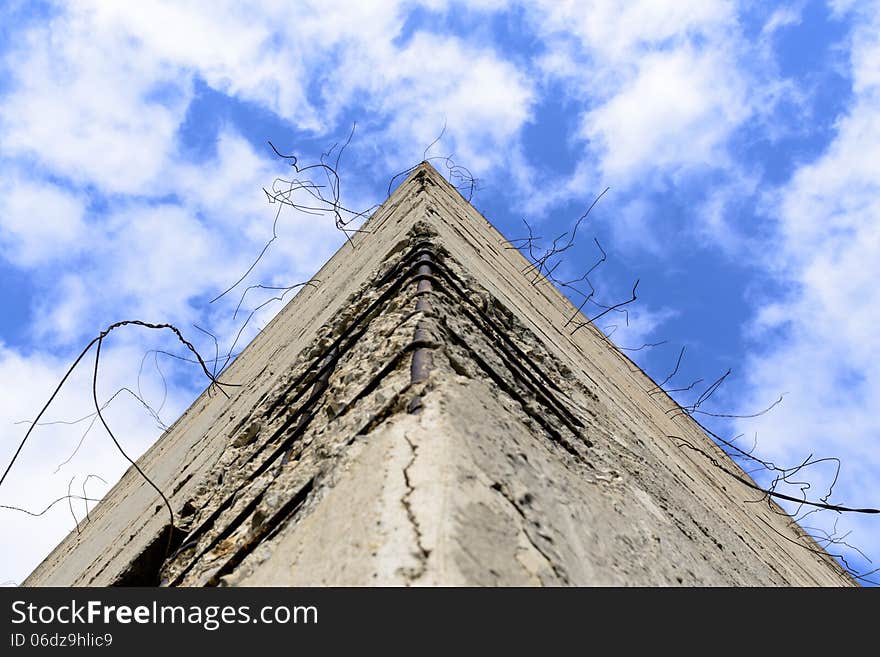 Fragment of old obsolete reinforced concrete structures with rusty iron rods outside. The pyramid of concrete looks at the blue sky.