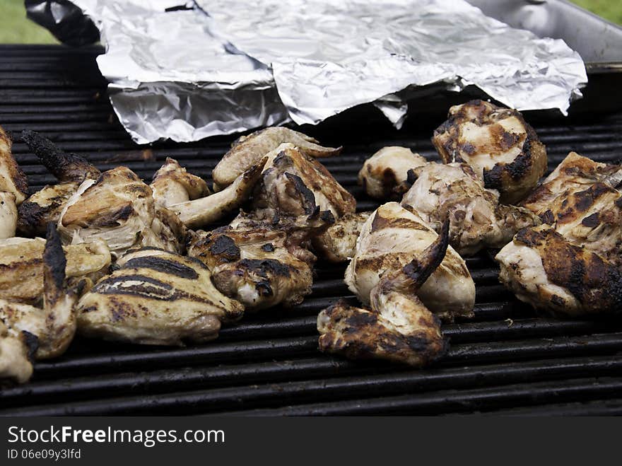 Chicken on an outdoor grill with a silver foil covered pan in the background. Chicken on an outdoor grill with a silver foil covered pan in the background