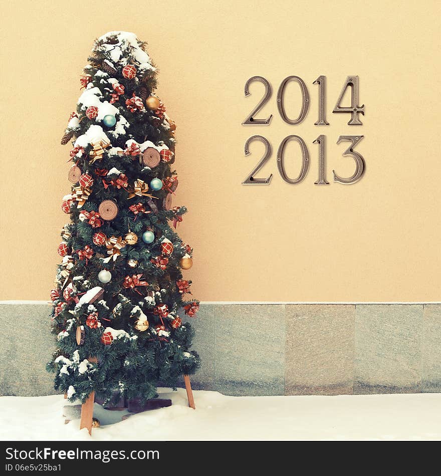 Cozy snowed Christmas tree in front of yellow wall outdoors