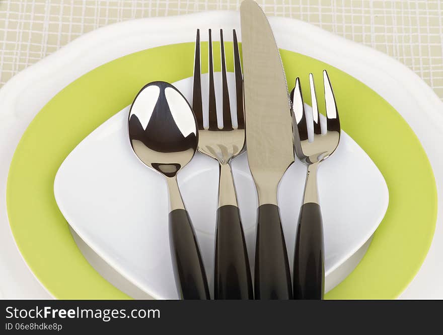 Elegant Table Setting with Spoon, Fork, Table Knife and Dessert Fork on White and Green Plates closeup