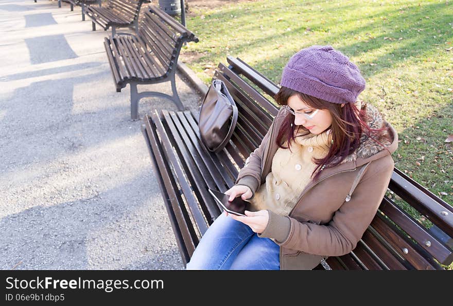 Young girl sitting on a bench and using her digital tablet outdoor in a park. Young girl sitting on a bench and using her digital tablet outdoor in a park.