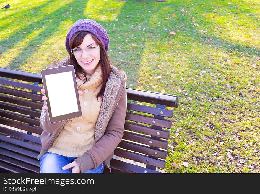 Young girl sitting on a bench and showing digital tablet outdoor in a park. Young girl sitting on a bench and showing digital tablet outdoor in a park.