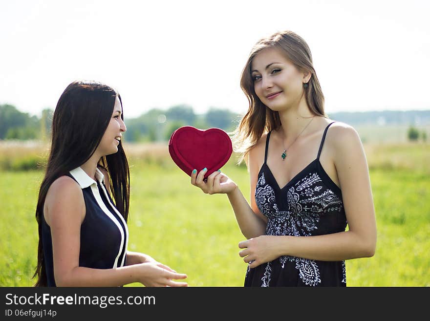 Two pretty women in love with red heart in sunshine summer field