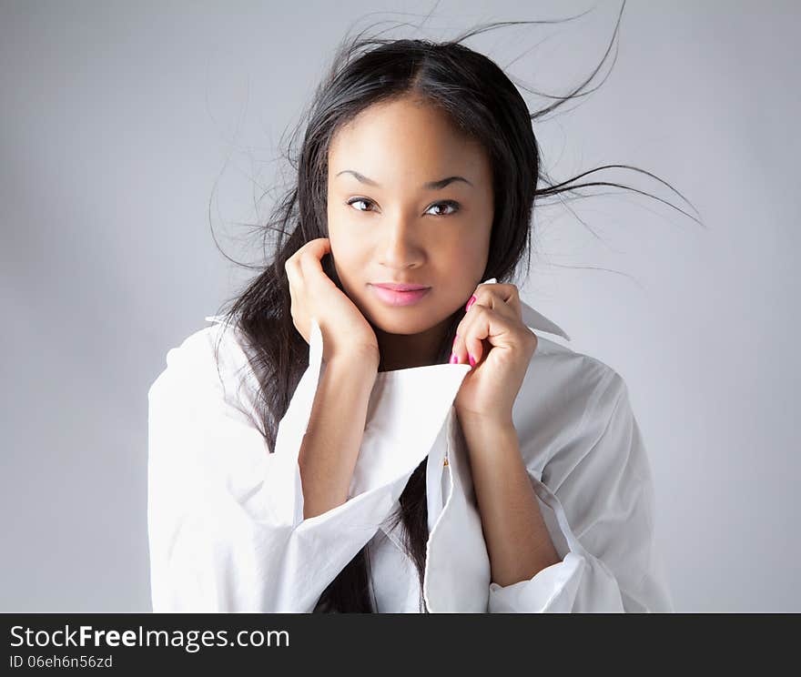 A portrait of a young African American and Thai woman with blowing hair looking flirtatiously at the viewer. A portrait of a young African American and Thai woman with blowing hair looking flirtatiously at the viewer