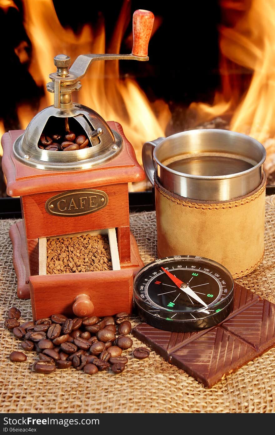 Coffee grinder and mug are near campfire beside them chocolate and compass. Coffee grinder and mug are near campfire beside them chocolate and compass