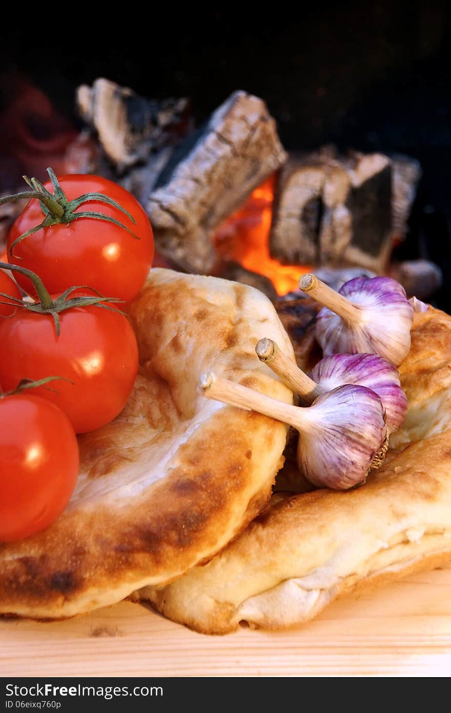 Bread, tomatoes and garlic on the background of hot coals. Bread, tomatoes and garlic on the background of hot coals