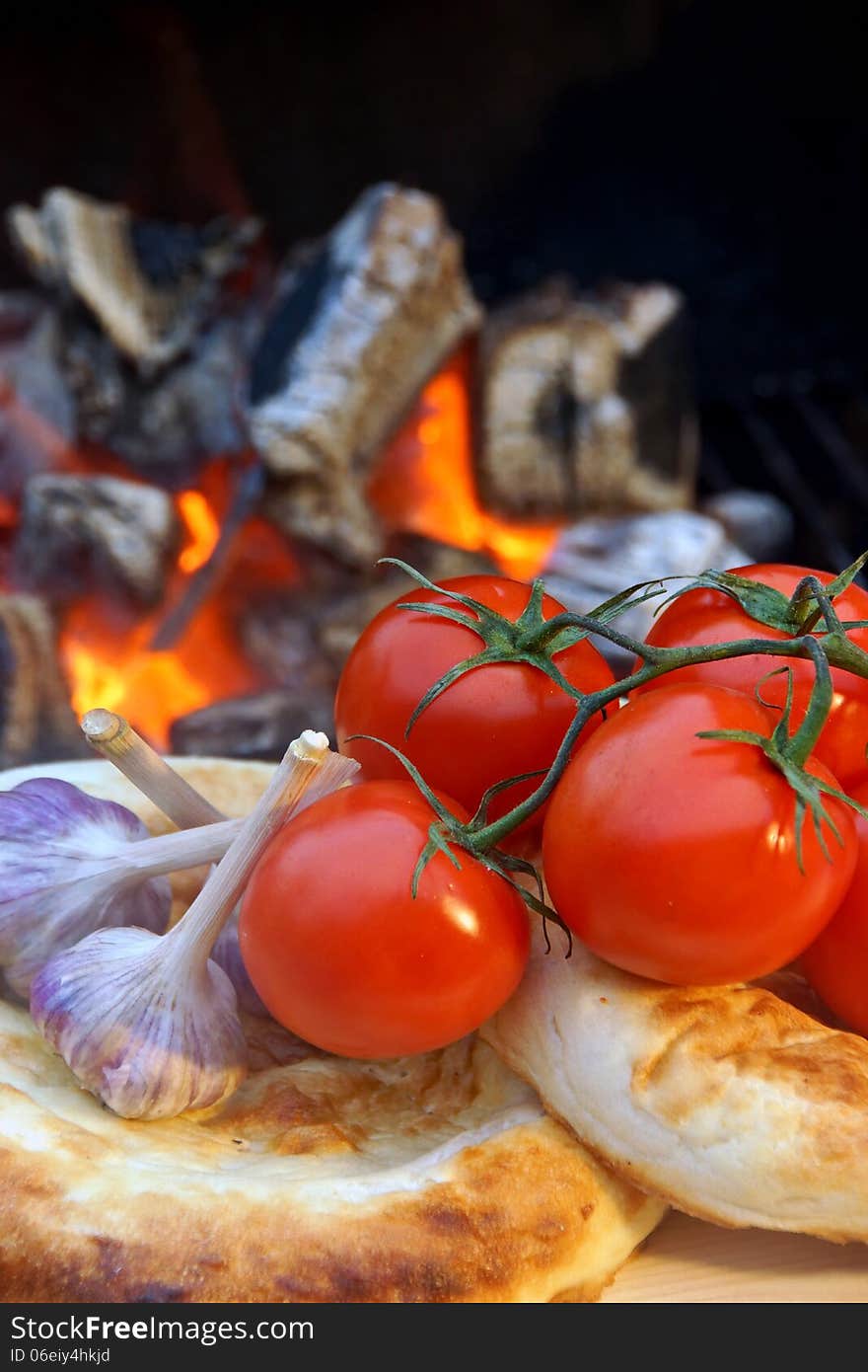 Bread, tomatoes and garlic on the background of hot coals. Bread, tomatoes and garlic on the background of hot coals