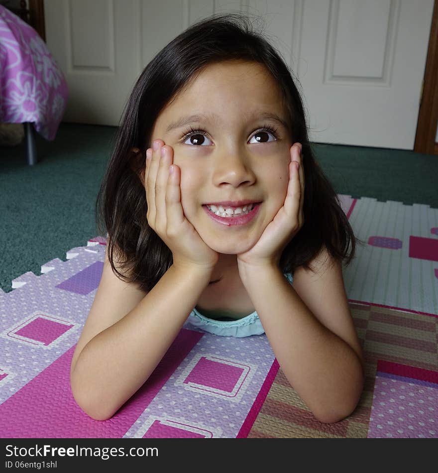 A young Asian girl smiles as she lies on her bedroom floor with her head resting in her hands. A young Asian girl smiles as she lies on her bedroom floor with her head resting in her hands.