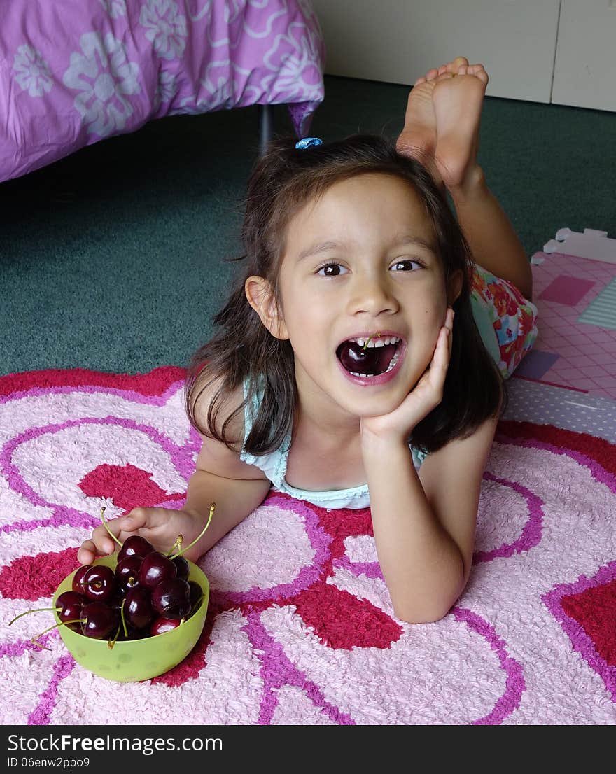 A young Asian girl relaxes on her bedroom floor and enjoys eating fresh cherries. A young Asian girl relaxes on her bedroom floor and enjoys eating fresh cherries.