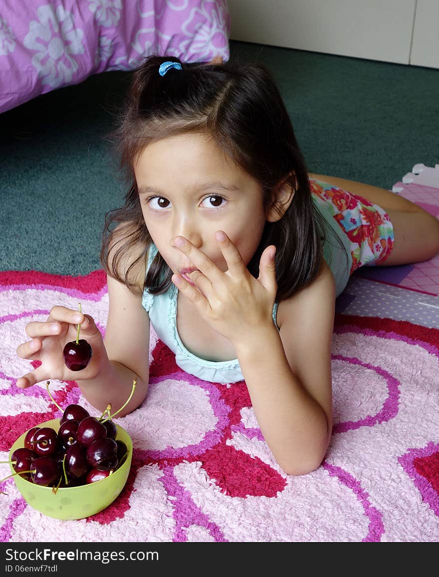 A young Asian girl lies on her bedroom floor as she licks the cherry juice from her fingers. She holds another cherry ready to eat. A young Asian girl lies on her bedroom floor as she licks the cherry juice from her fingers. She holds another cherry ready to eat.