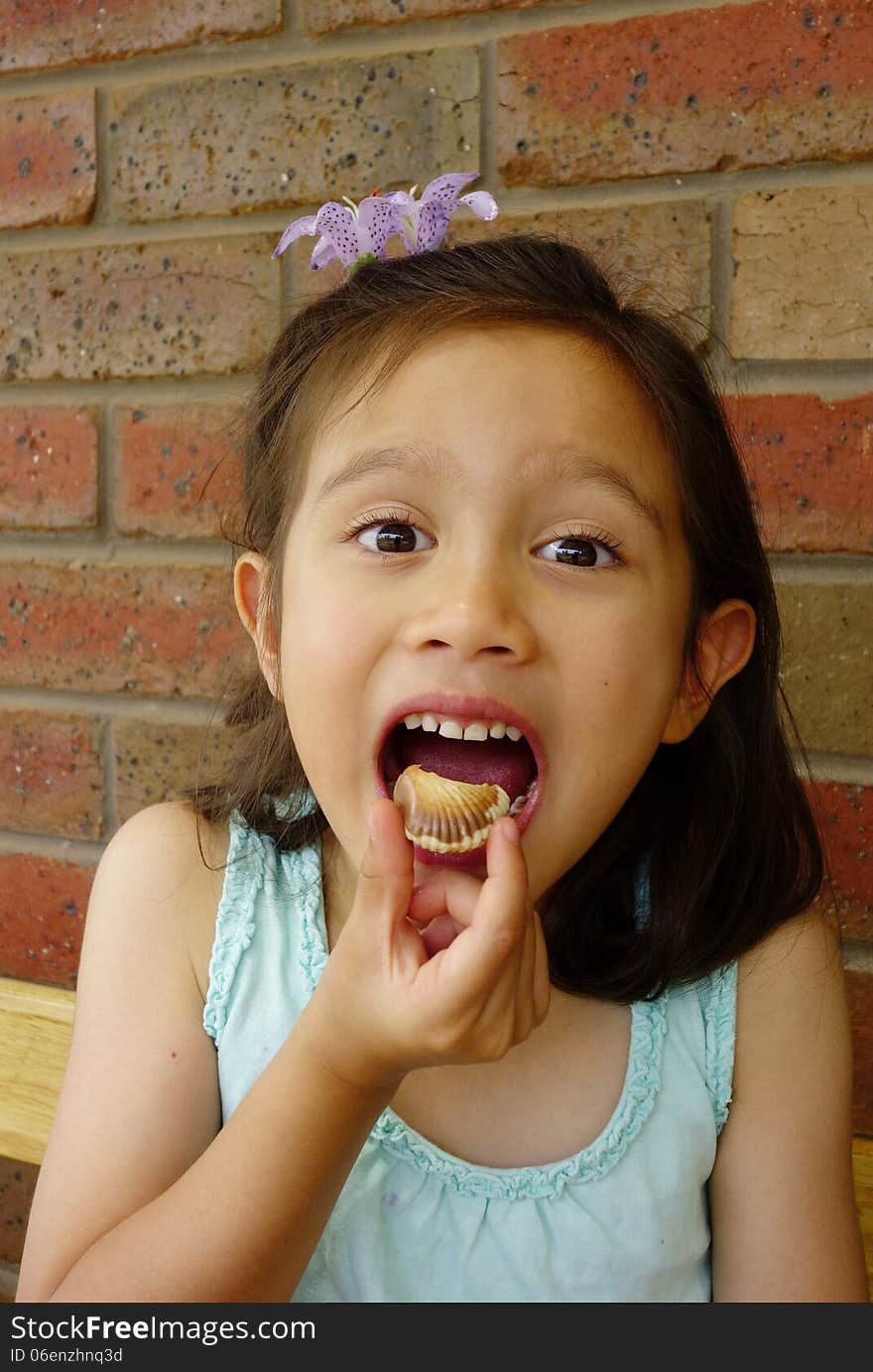 A young Asian girl delights in the thought of eating the chocolate she holds in her fingers. A young Asian girl delights in the thought of eating the chocolate she holds in her fingers.