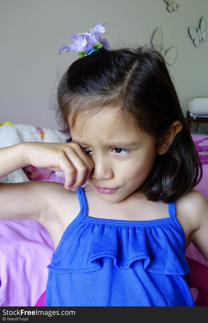 A young Asian girl appears upset and sad as she rubs her right eye. A young Asian girl appears upset and sad as she rubs her right eye.