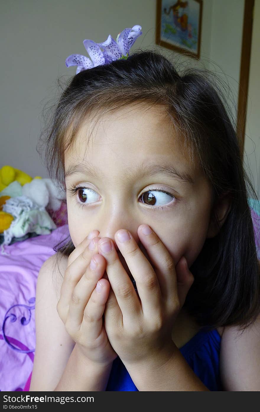 A frightened young Asian girl holds her hands over her mouth as she stares with her eyes wide open. A frightened young Asian girl holds her hands over her mouth as she stares with her eyes wide open.