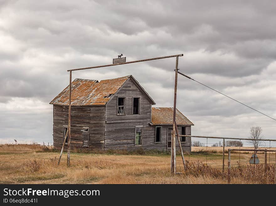 Old abandoned grey wooden house sitting under a cloud filled sky on a cool autumn day.The driveway entrance structure has a little wooden terrier perched on top. Old abandoned grey wooden house sitting under a cloud filled sky on a cool autumn day.The driveway entrance structure has a little wooden terrier perched on top